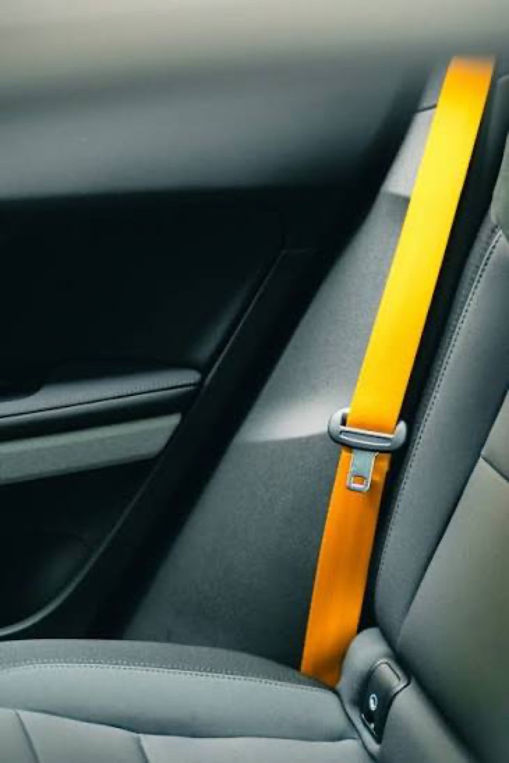 Bright orange seatbelt webbing fitted in a grey vehicle interior, routed past the door pillar down towards the seat.