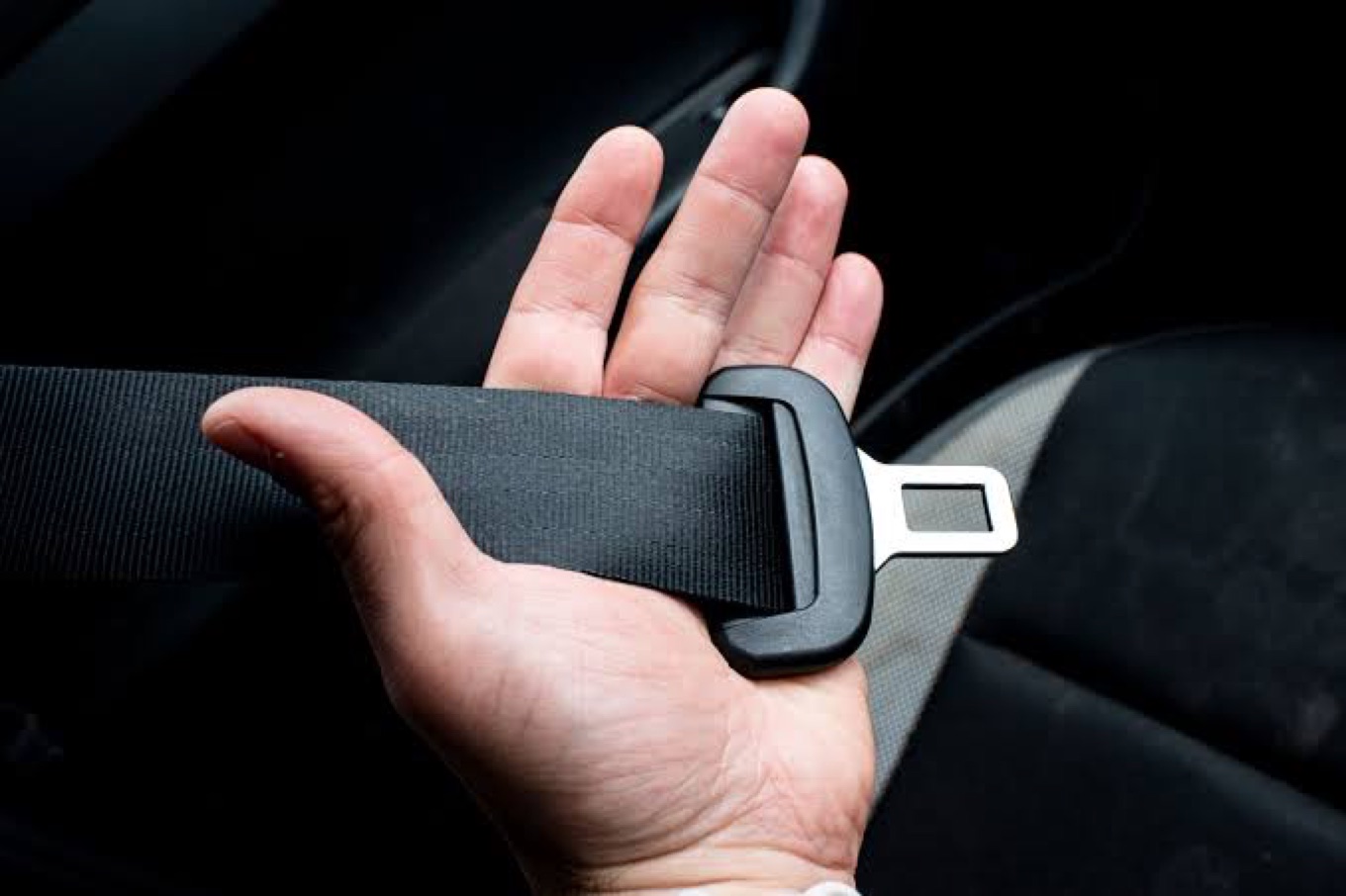 An open palm supporting a length of black seatbelt webbing with the metal-tipped tongue resting across the fingers.