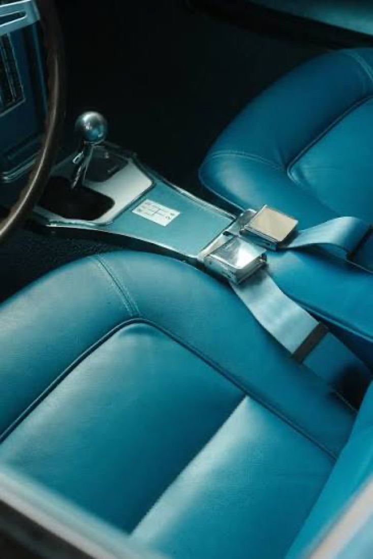 Blue-trimmed vehicle interior showing a metal seatbelt buckle and latch resting between two seats beside the gear lever.
