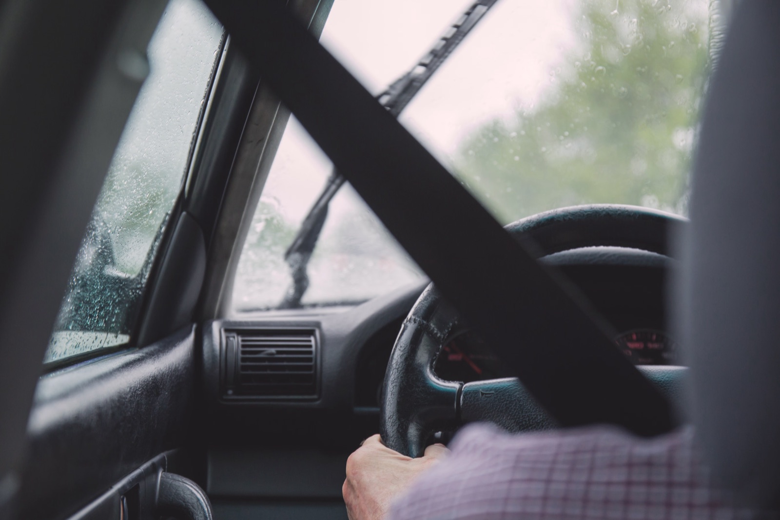 View from the driver's seat of a vehicle with the shoulder belt running diagonally across the frame past the steering wheel on a rainy day.